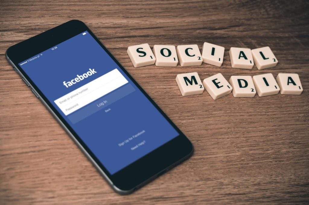 Leżący na stole smartfon z wyświetloną na nim aplikacją Facebook oraz ułożonym z klocków napisem social media 